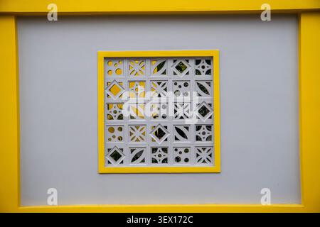 Decorative white concrete breeze block panel with geometric patterns in a yellow frame on grey wall Stock Photo
