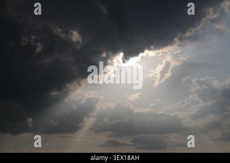 Powerful sunlight breaking through dark storm clouds, creating striking crepuscular rays in a dramatic sky before the rain. Stock Photo