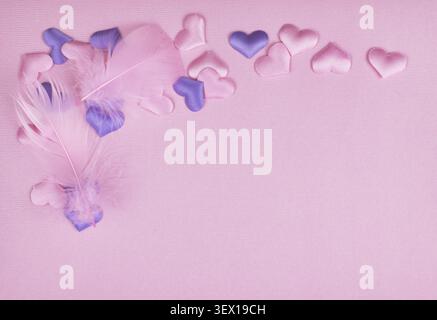 Feathers and pink and purple satin hearts in a cornar arrangement on paper texture for Valentine Day background Stock Photo