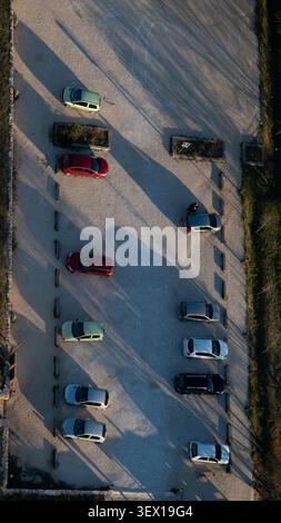 Cars parked in rows on a gravel lot casting long shadows at sunset from an aerial view Stock Photo