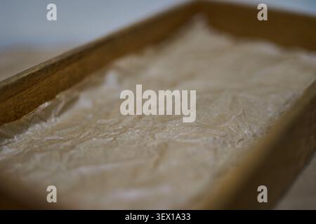 Wooden Tray Lined With Crumpled Parchment Paper Placed On Table Closeup Showing Paper Texture And Wood Grain With Shallow Depth Of Field For Serving Or Packaging Display. Stock Photo