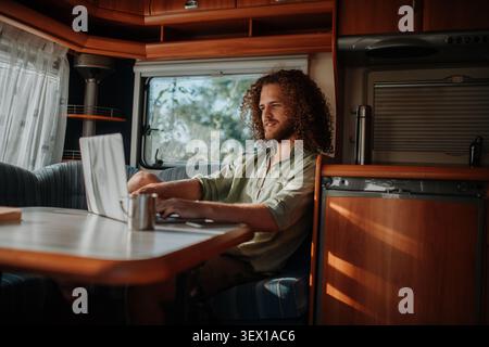 Young man working remotely from caravan. Man using camper as homeoffice, working on notebook. Stock Photo