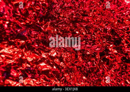 A crumpled red foil material, showcasing its intricate texture and vibrant reflective surface. Stock Photo