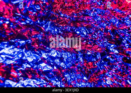 A close-up, abstract depiction of crinkled metallic foil illuminated with vibrant blue and red lights. Stock Photo