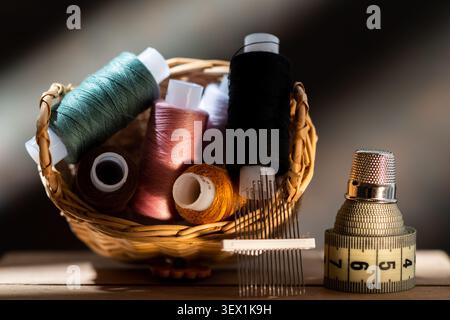 Wicker basket with colorful sewing threads, needles, measuring tape and thimble on a wooden table. Stock Photo