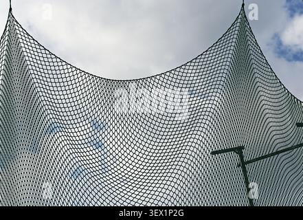 A minimalist upward-looking view of a suspended protective net silhouetted against a cloudy sky. The geometric mesh pattern creates an abstract compos Stock Photo