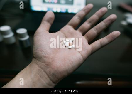 Hand holding white pills on dark desk with medicine bottles and blurred screen in background — Stock Photo