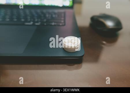 Small white pill container resting on black laptop keyboard edge beside wireless mouse on wooden Stock Photo