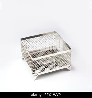 An empty square silver metal mesh basket with decorative legs, captured from a high angle in bright studio light against a clean white background Stock Photo