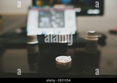 Close-up of three stacked plastic bottle caps on glossy black table with blurred laptop in Stock Photo