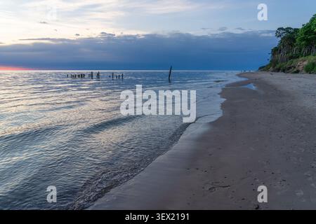 Old wooden pier remains on the Baltic Sea shoreline beneath dramatic storm clouds near Staldzene cliffs, Ventspils, Latvia Stock Photo