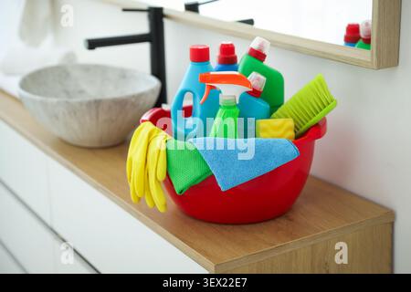 Red plastic basin with cleaning products and supplies on counter in bathroom Stock Photo