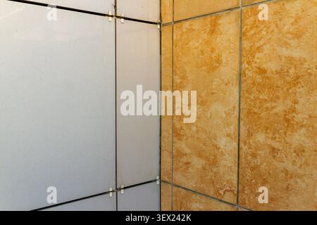 Close-up view of building facade installation showing contrasting white composite panels and orange marble texture porcelain tiles. Stock Photo