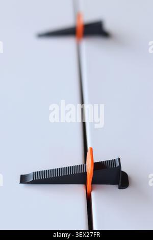 Tile leveling system, orange base and black wedge installed between two ceramic tiles to ensure a flat surface and uniform joints. Tile laying process Stock Photo