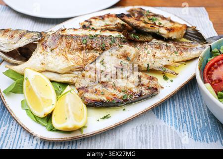 Grilled whole fish served with lemon wedges and fresh herbs. Mediterranean seafood background for restaurant menus healthy meals and home cooking. Stock Photo