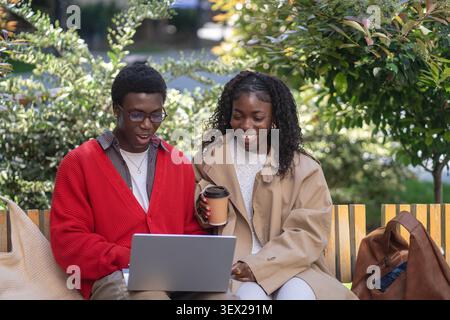 Cheerful smiling african american couple man and woman students spending time working on laptop. Stock Photo