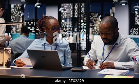 Two staff members reading emails and solving tasks together on laptop at desk, office workers analyzing data on notebook. Accounting work and interpreting statistical information. Stock Photo