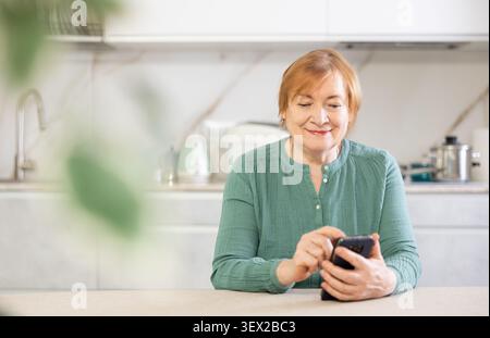 Smiling older woman sending messages using smartphone with someone on her phone Stock Photo