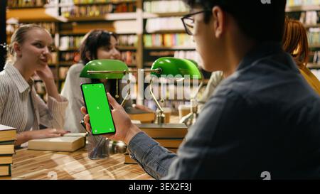 Isolated green screen on laptop near study group at library desk, learning environment with green lamps at wooden table. Creating editable screen space for learning content. Stock Photo