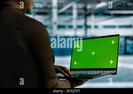 System operator uses a green screen laptop in a data center for hardware diagnostics, screen replacement, and server workflow monitoring. Stock Photo