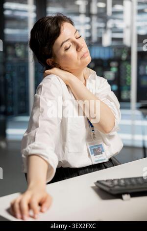 Exhausted server room worker handles fatigue in a data center after a long hardware troubleshooting session at a computer workstation. Stock Photo