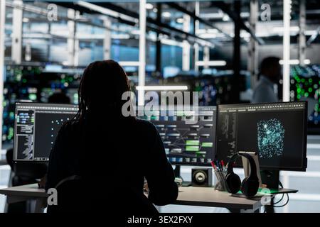 Data center engineer uses a desktop computer in a data center to manage AI visualization and optimize server infrastructure. Stock Photo