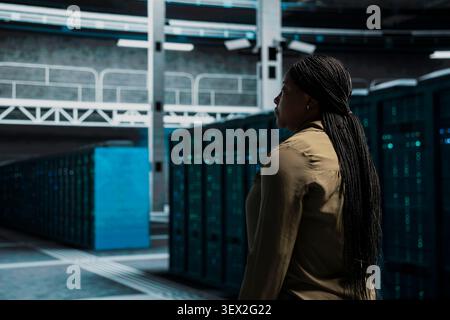 Team supervisor walking in data infrastructure center with supercomputers supporting business needs with supervisor doing checkup. Stock Photo