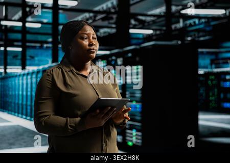 System administrator uses a digital tablet in a data center to run hardware diagnostics and maintain operational stability. Stock Photo
