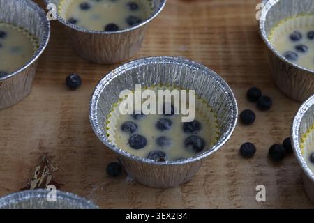 Paper baking cups filled with blueberry muffin batter before baking. Homemade muffins prepared in disposable baking molds on a wooden kitchen table. Stock Photo