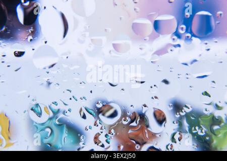 Raindrops gather on a glass surface. Colored reflections blur behind the droplets. Soft bokeh highlights create a dreamy atmosphere. Water beads form Stock Photo