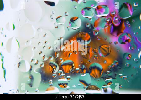 Water droplets distort a colorful, abstract background. Shapes float within the droplets, forming abstract patterns. Light refracts through the water, Stock Photo