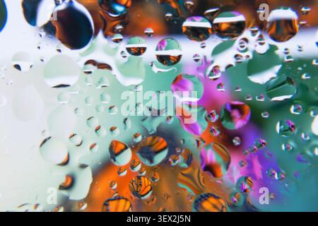 Raindrops cling to a colorful, reflective surface with floral colors. Light refracts through each droplet, creating vivid reflections. Colors swirl be Stock Photo