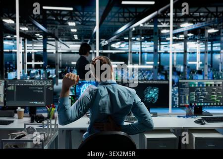 Technician stretches at a workstation in a server farm to relieve back fatigue after long technical work. Stock Photo