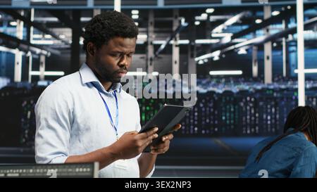Data center technician uses a tablet with node tree programming to optimize resource allocation and analytics. Stock Photo