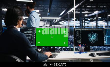 Technician programs on a green screen computer in a data center with generative AI assistance. Stock Photo