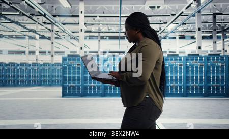 Smiling data center engineer uses a laptop after reducing downtime through disaster recovery planning. Stock Photo