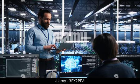 Computing facility IT technician working with notebook to track neural network AI large language model visualization with in high tech facility working with notebook to oversee servers powering. Stock Photo
