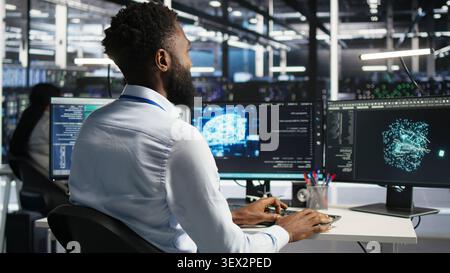 Computing hub engineering team interprets AI generated data analytics graphs, while teamworking server facility team members working with AI program showing predictive system metrics. Stock Photo