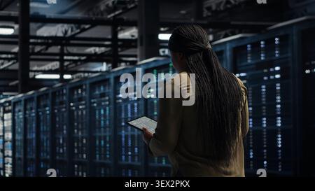 Data center technician uses a tablet in a server room to manage infrastructure and support reliable technology operations. Stock Photo