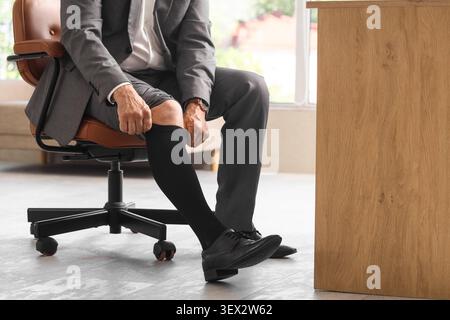 Businessman putting on black socks in office chair Stock Photo