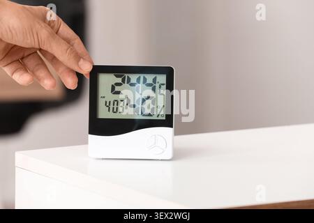 Hand adjusting digital thermometer and hygrometer on table Stock Photo
