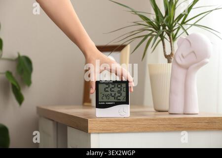 Hand adjusting digital temperature and humidity meter on wooden table Stock Photo