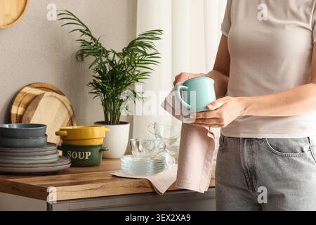 Person drying a turquoise mug in a kitchen Stock Photo