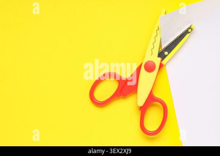 Decorative craft scissors cutting white paper on yellow background Stock Photo