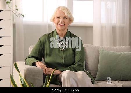 Beautiful senior woman sitting on sofa at home Stock Photo