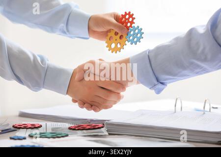 Male engineers with gears shaking hands in office, closeup Stock Photo