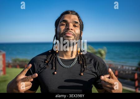 Young man showing peace sign by ocean Stock Photo