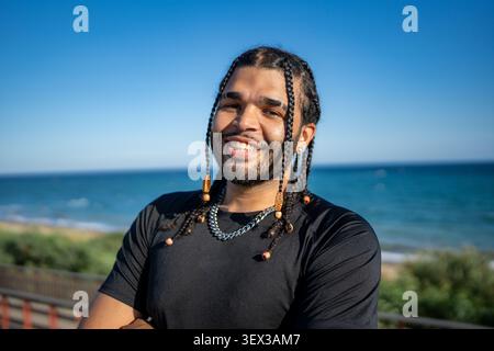Smiling young man with braided hair by the sea Stock Photo