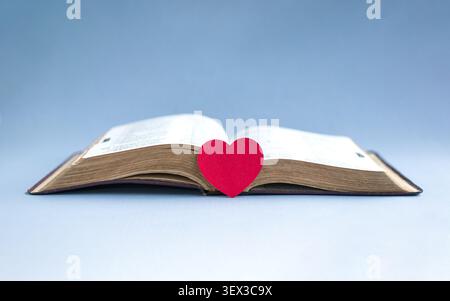 Red paper heart with open holy bible. Isolated on light blue background. Stock Photo