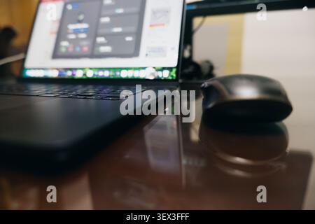 Black laptop and wireless mouse on glossy desk with blurred background — modern workspace setup in Stock Photo